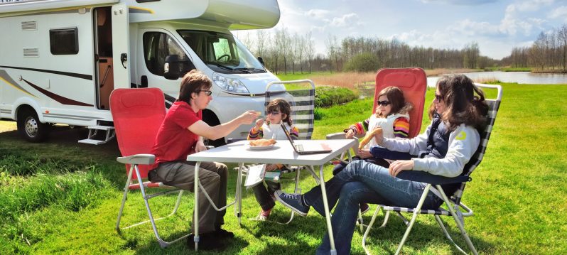Family vacation, RV (camper) travel with kids, happy parents with children sit at the table in camping on holiday trip in motorhome